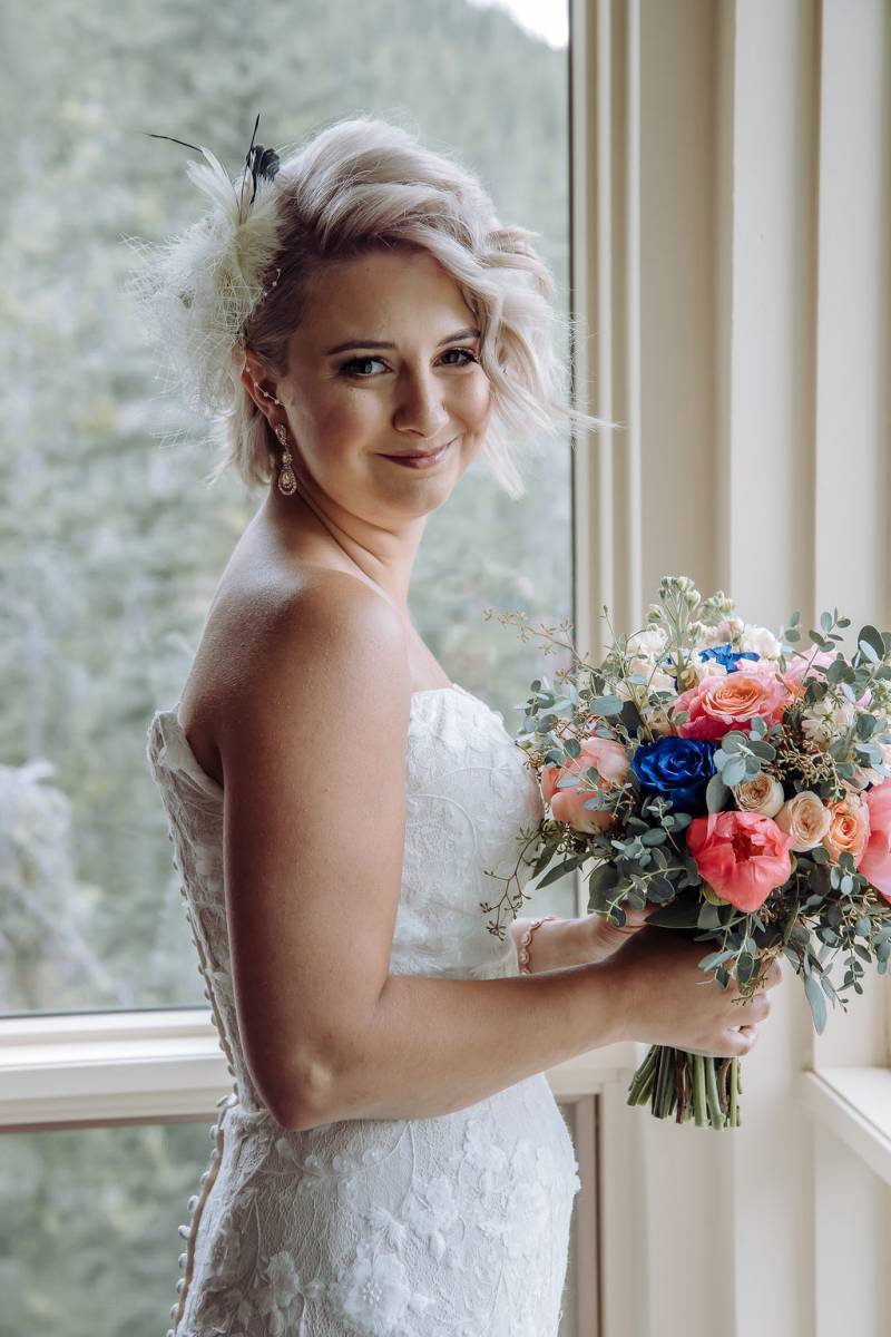 Bride holding blue pink and blsuh bouquet wearing white lace dress smiling 