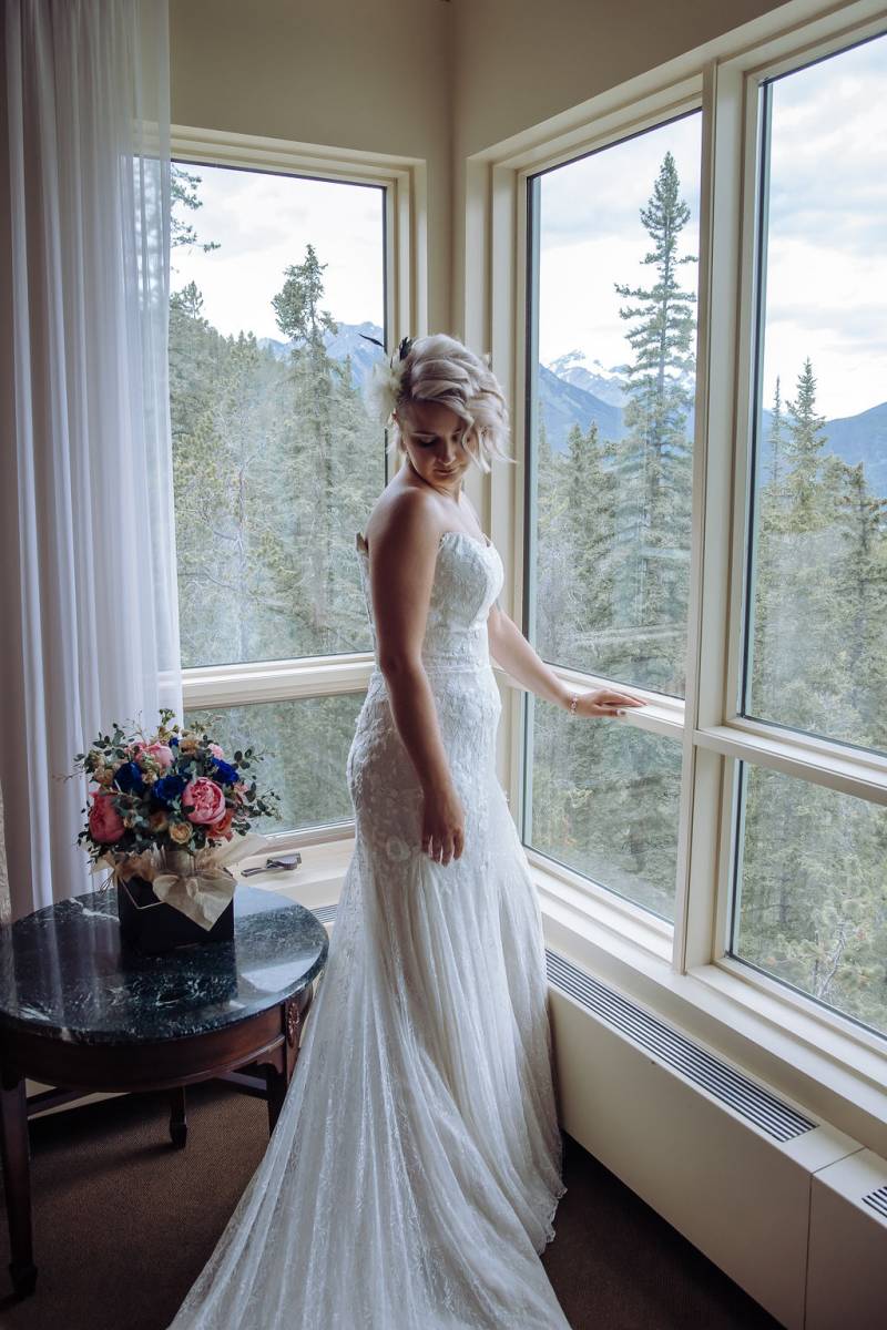 Bride standing in white dress at windowsill 