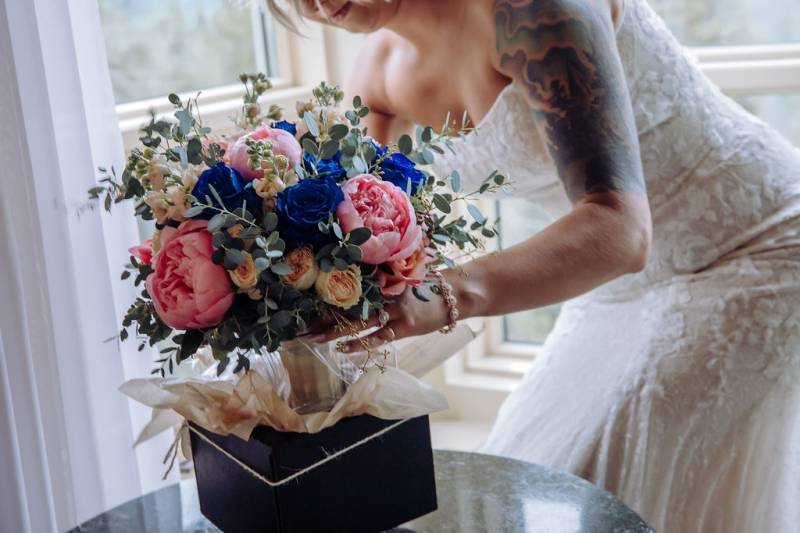Bide leaning over table picking up bouquet with pink blue and blush flowers