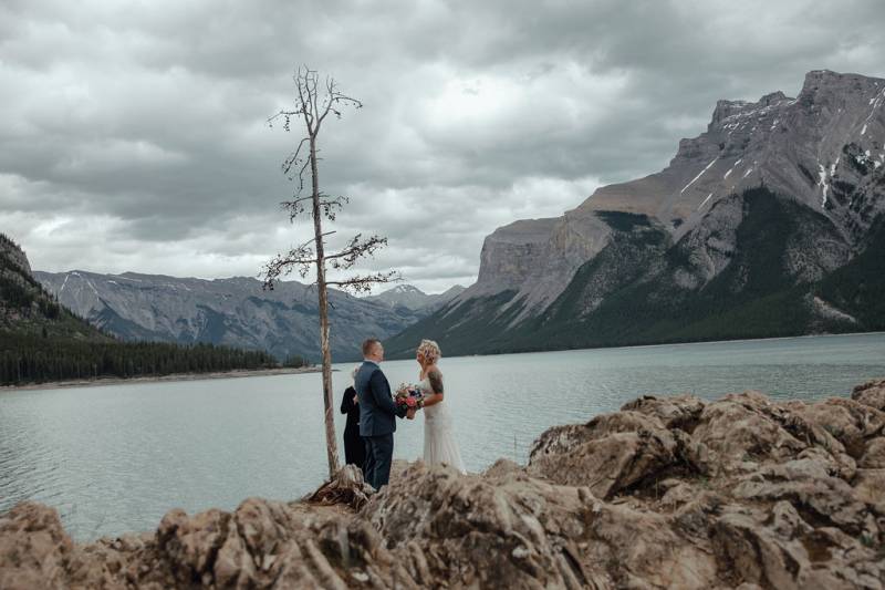 Bride and groom stand together overlooking lake and mountains 