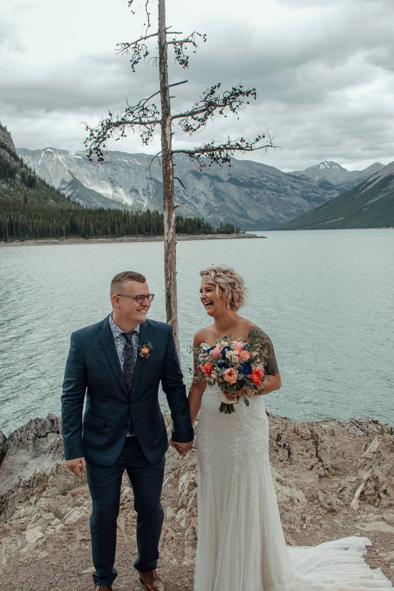 Bride and groom laughing holding hands overlooking lake and mountains 