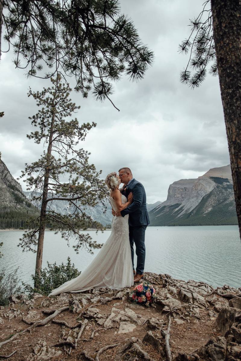Bride and groom kiss overlooking lake and mountains 