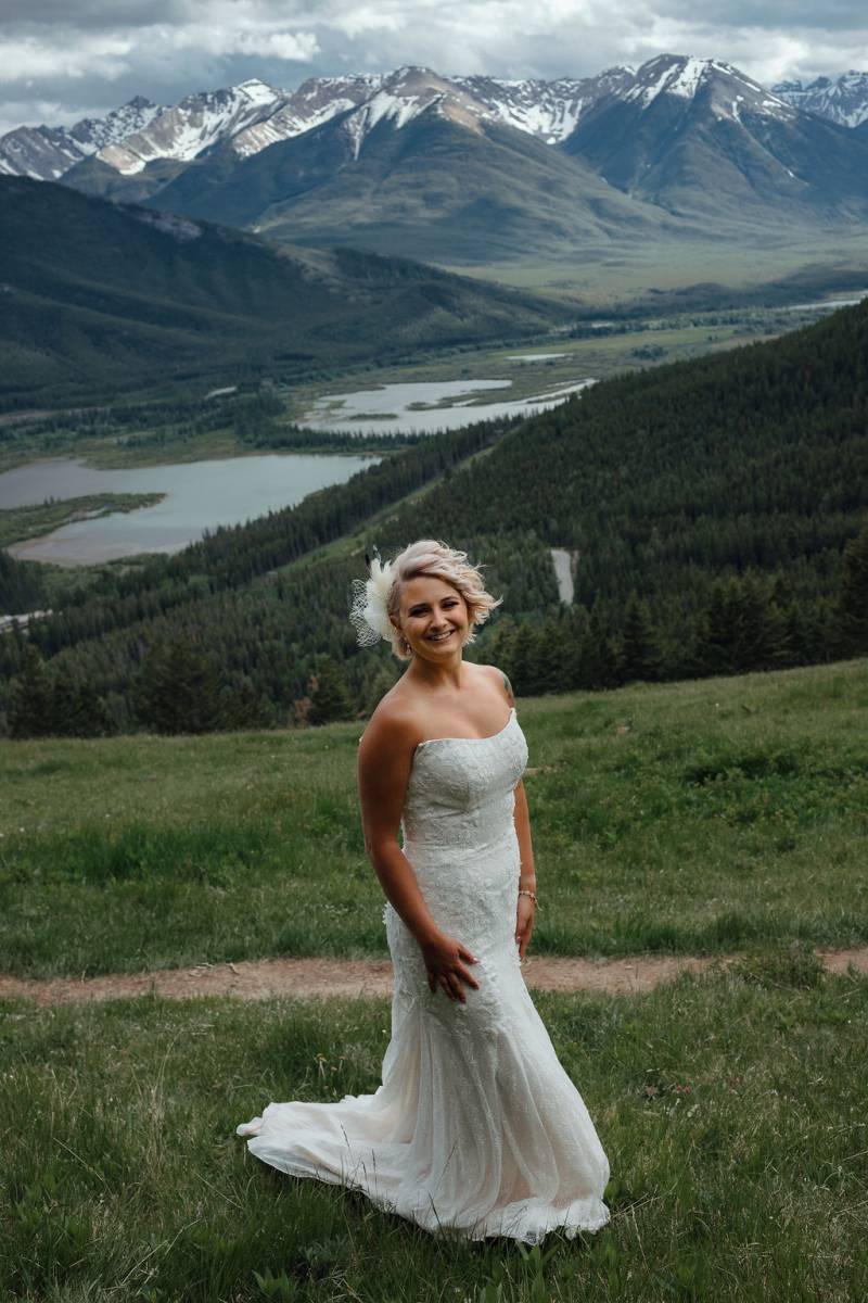 Bride standing on grassy hill overlooking mountains and lake 