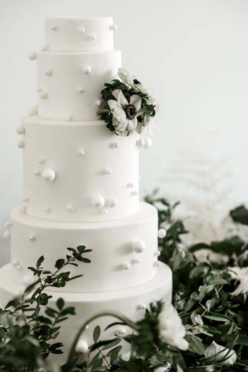 Large white wedding cake with white floral accents and greenery around 