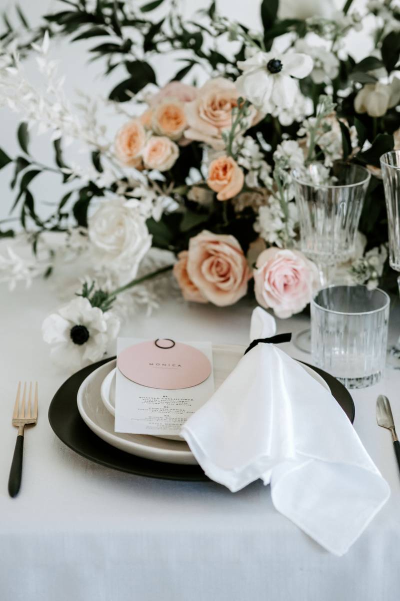 Table setting with black plates and white napkin and blush floral centerpiece 