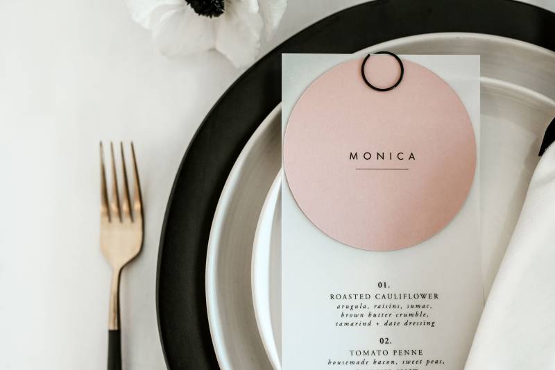 Place setting flat lay with gold cutlery and black plates with white and blush menu on top