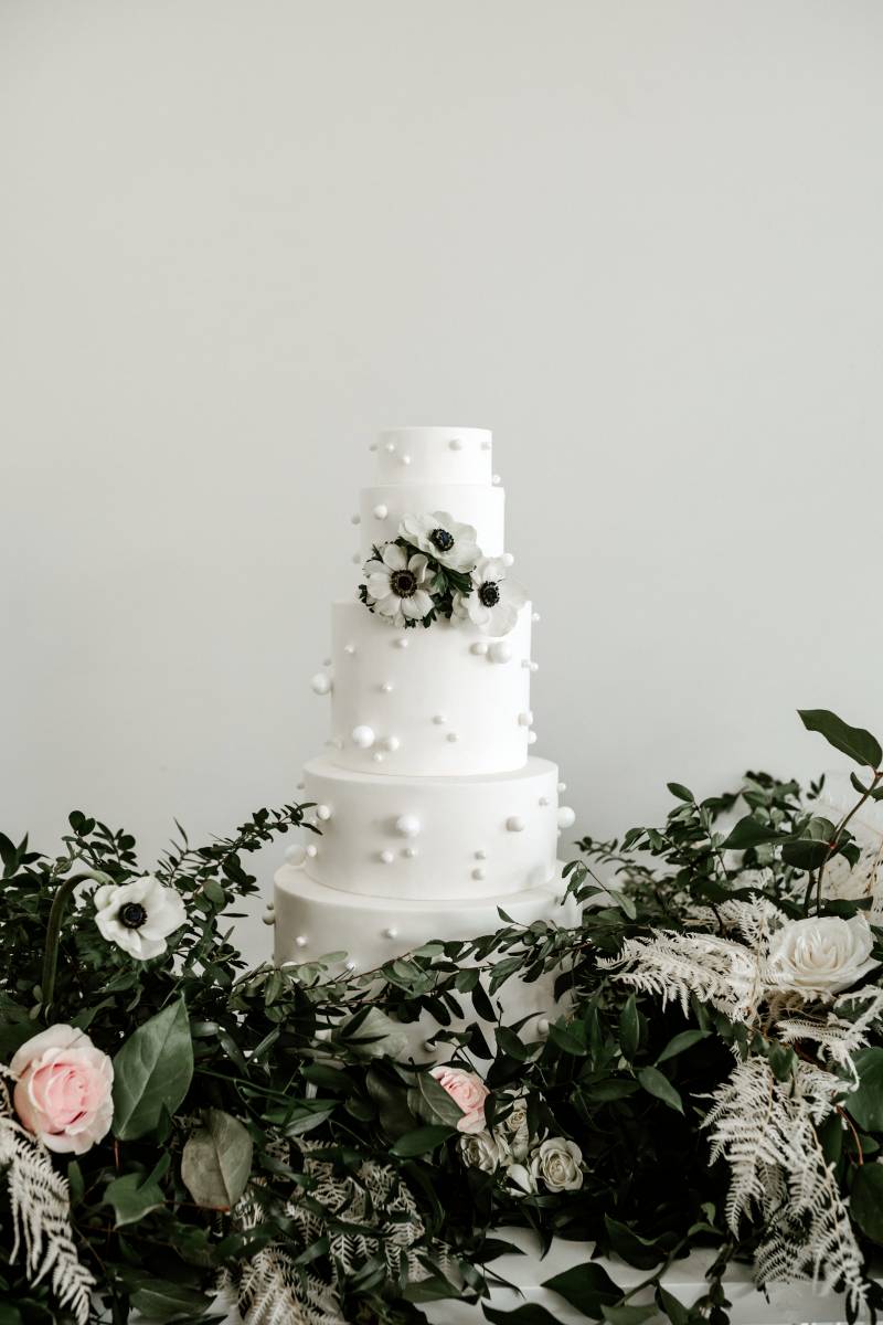 Large white wedding cake with white floral accents and greenery around 