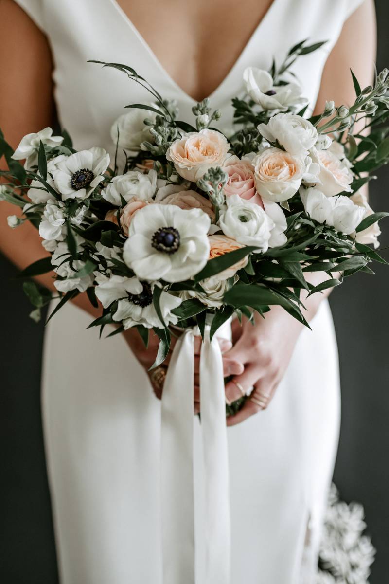 Woman in white lace dress holding blush and white bouquet and white ribbon 