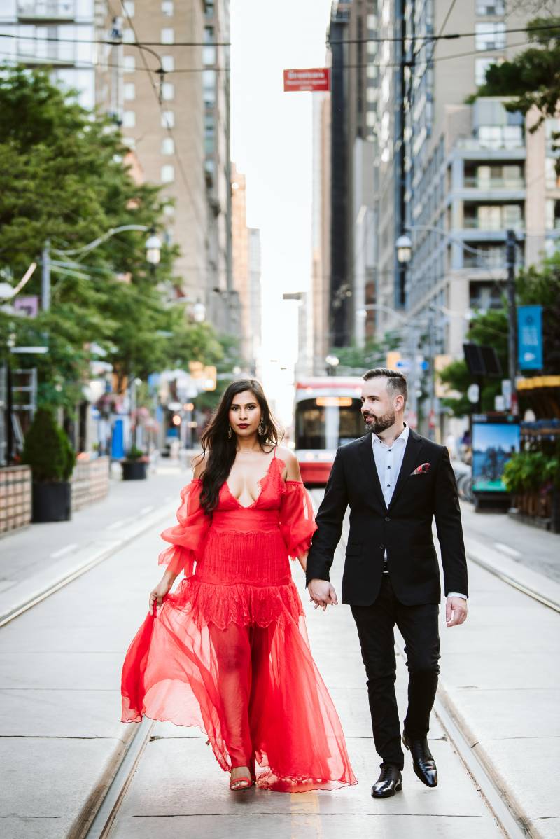 Bride walks in red dress holding hand of groom on train tracks 
