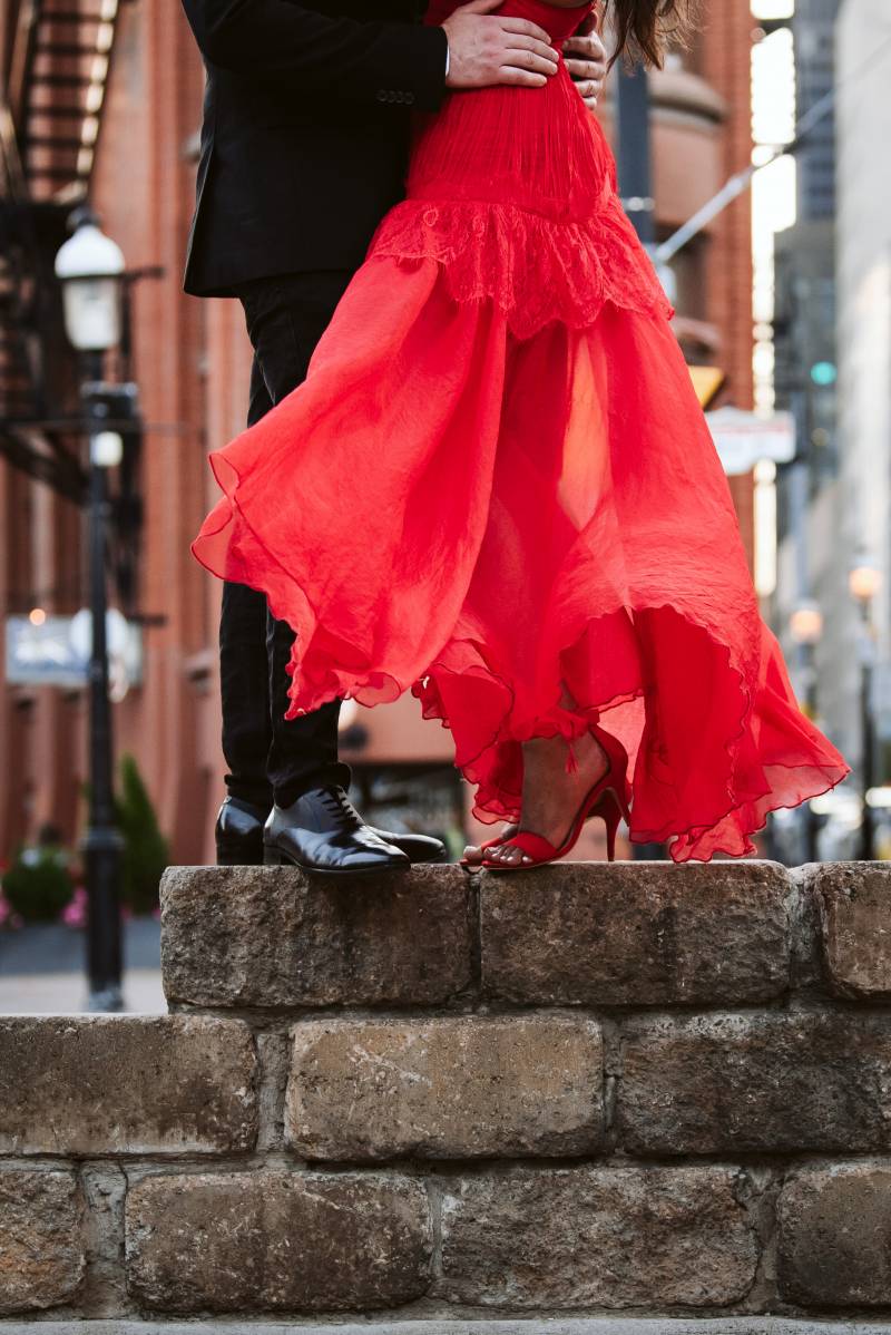 Bride and groom stand on concrete wall holding waist with city in background 