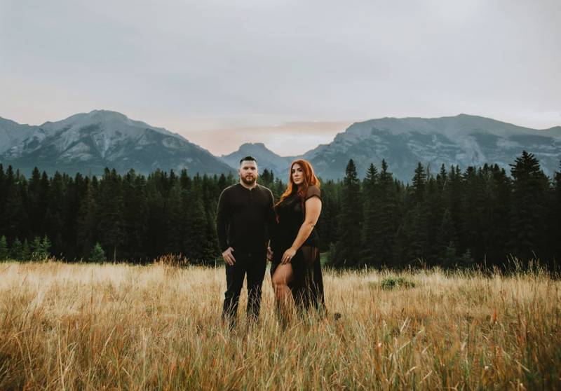 Man and woman stand in brown grassy field in front of mountains 