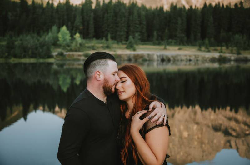 Man embraces woman eyes closed while mountains reflect behind 
