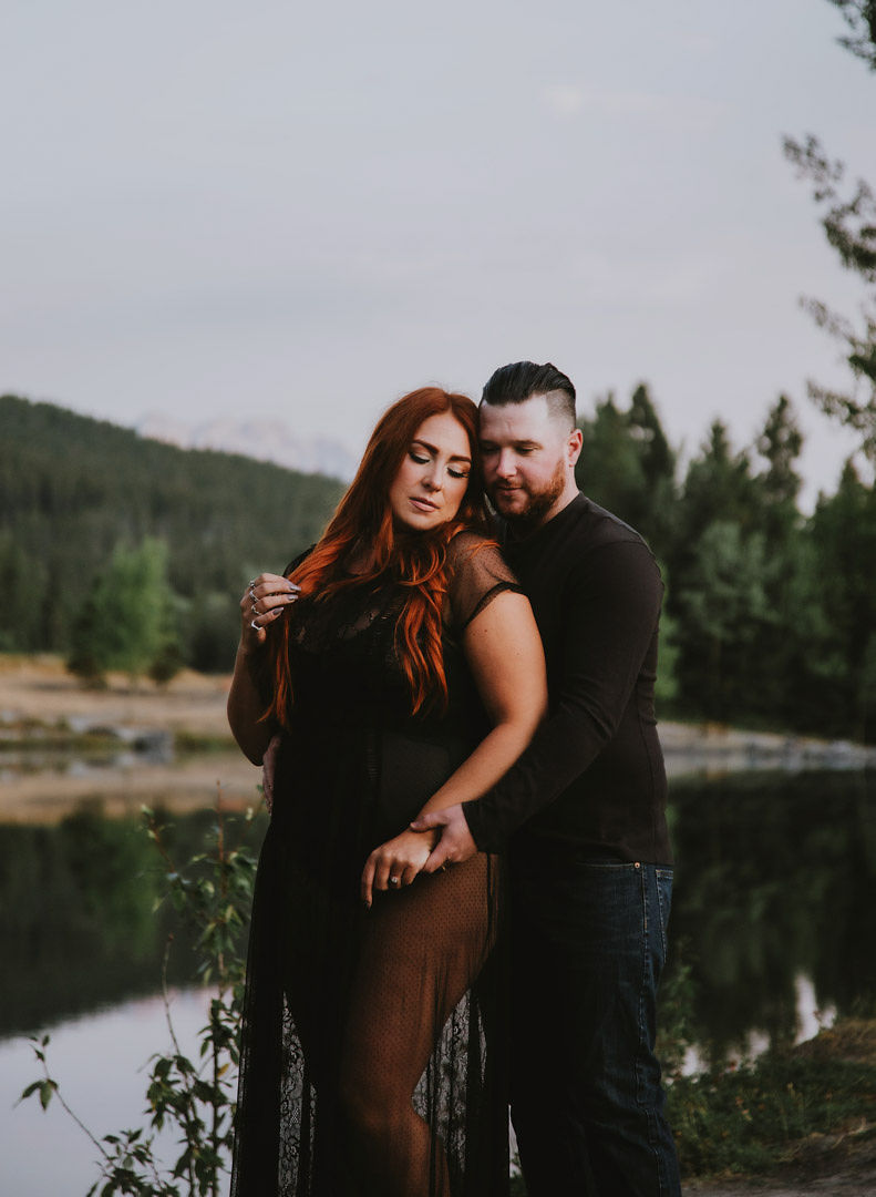 Man embraces woman from behind beside river and forest 