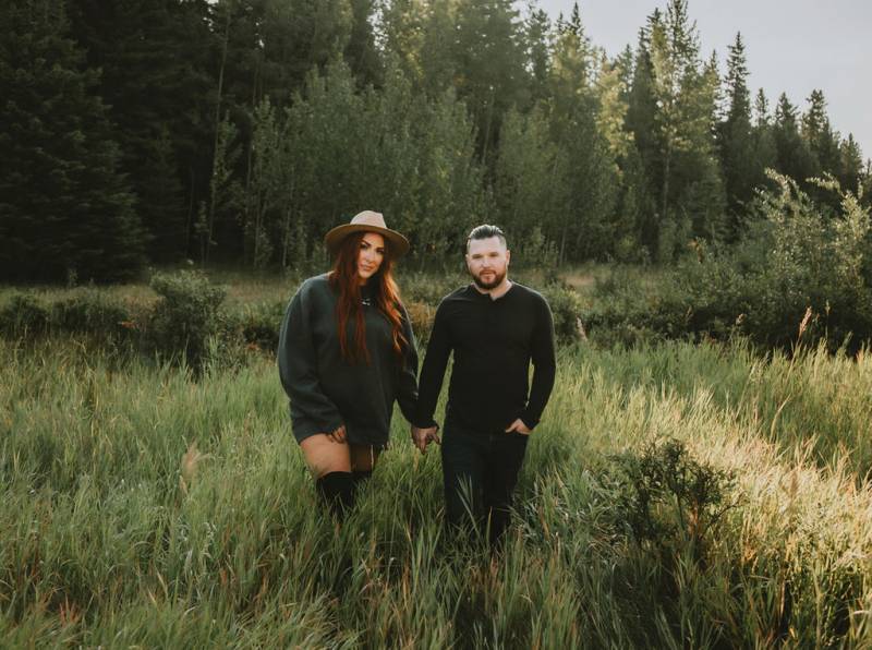 Man and woman walk holding hands in grassy forest field 