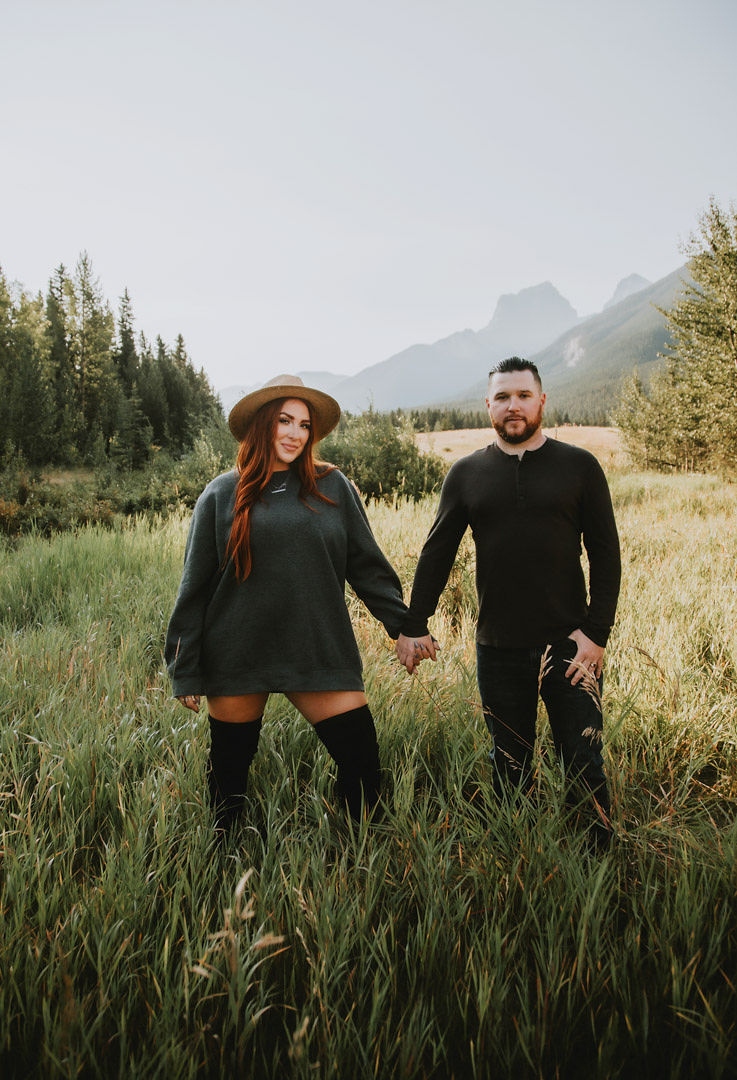 Man and woman stand holding hands in tall grassy field 