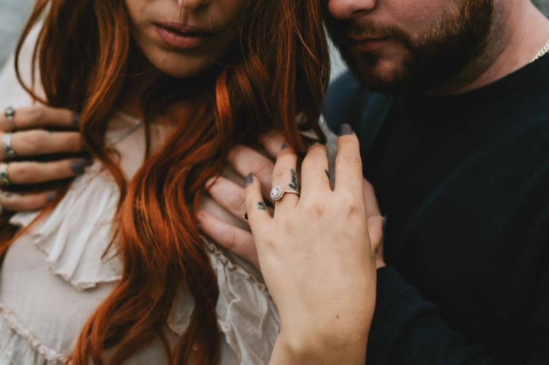 Man embraces woman from behind woman showing ring on shoulder 