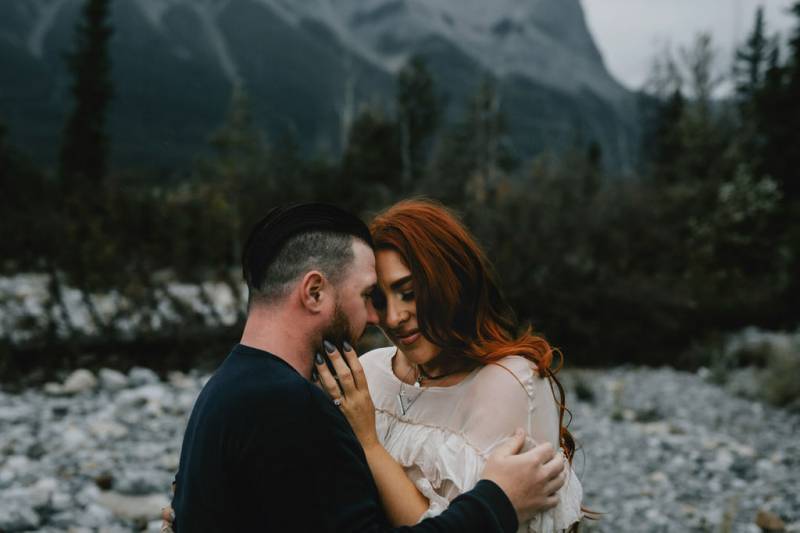 Man and woman touch foreheads embracing in forested area