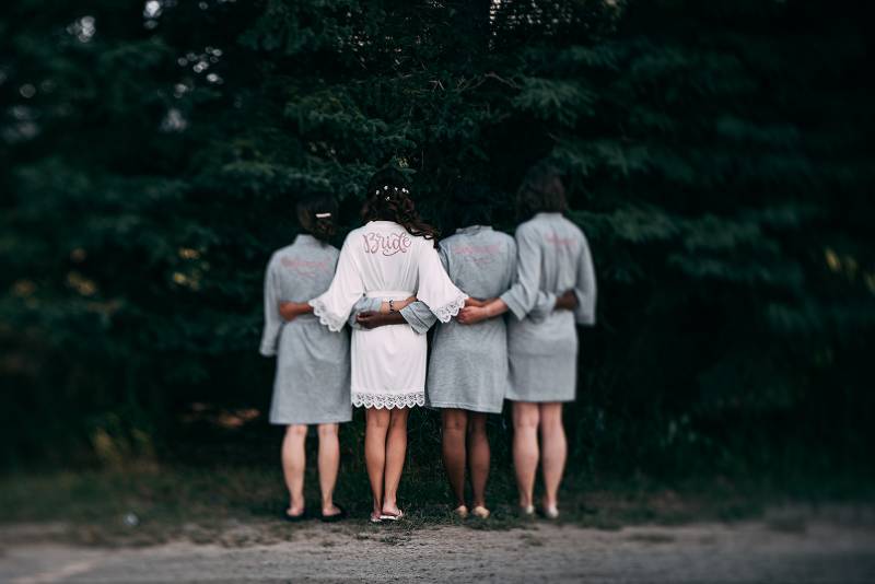 Bride stands in between bridesmaids arms around backs wearing bridal robes