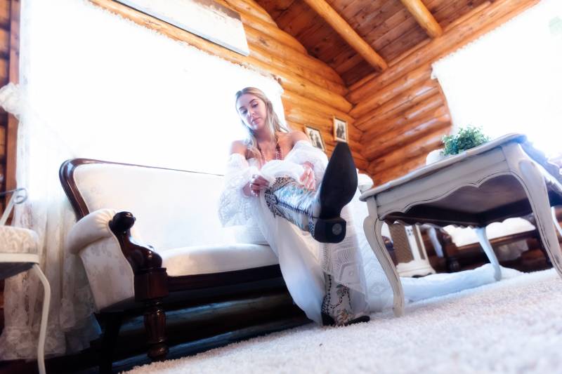 Bride sitting in white dress putting on cowboy boots 