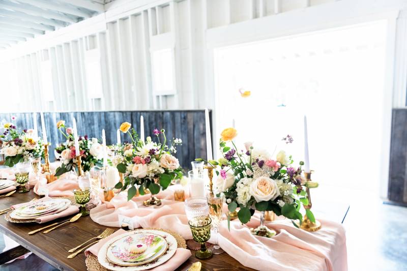 Table setting with gold cutlery and floral plates with yellow white and blush floral centerpieces 