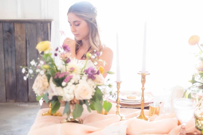 Bride sitting behind lavender and white flowers and table with peach table runner