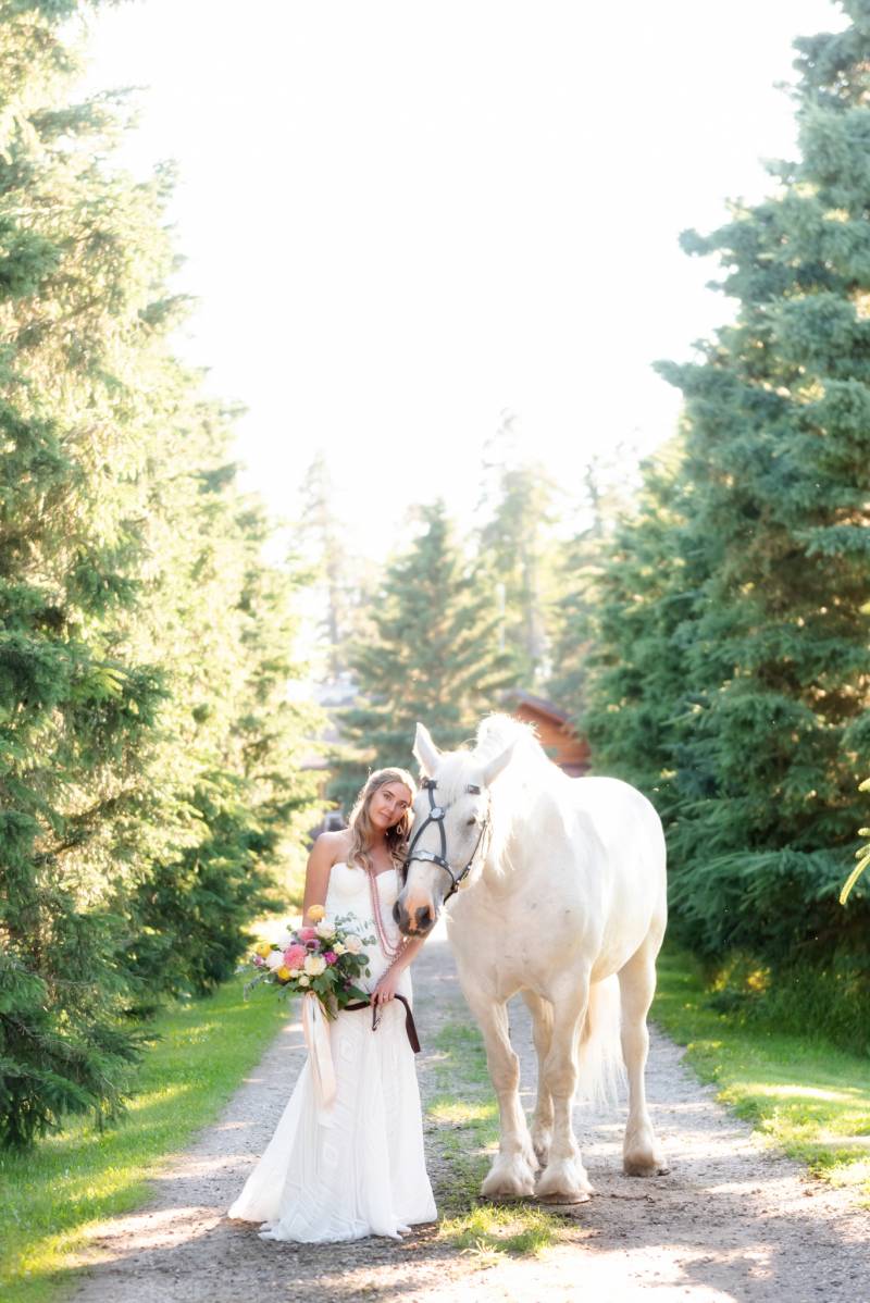 Bride standing on gravel path holding pink and white bouquet and horse 
