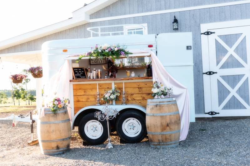 Mobile bar with barrels to the side in front of blue and white barn 