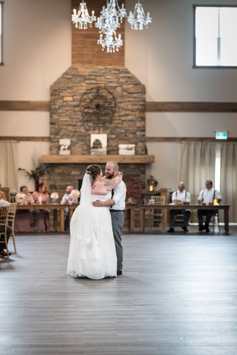 Bride and groom embrace dancing under crystal chandelier on wooden floor 