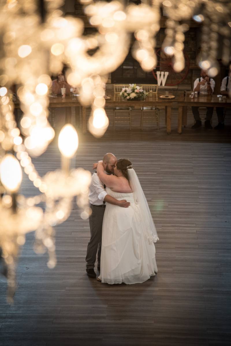 Bride and groom embrace dancing under chandelier on wooden floor 