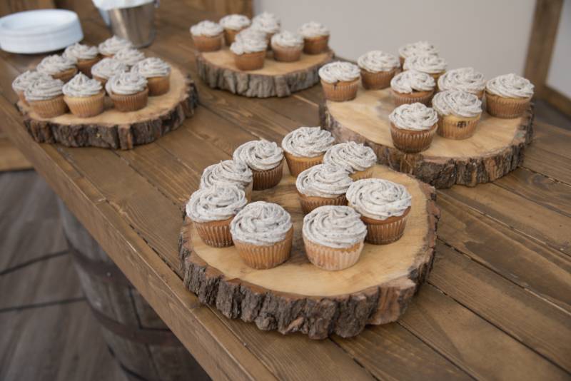 Four wooden platters of cupcakes with grey icing on wooden table 