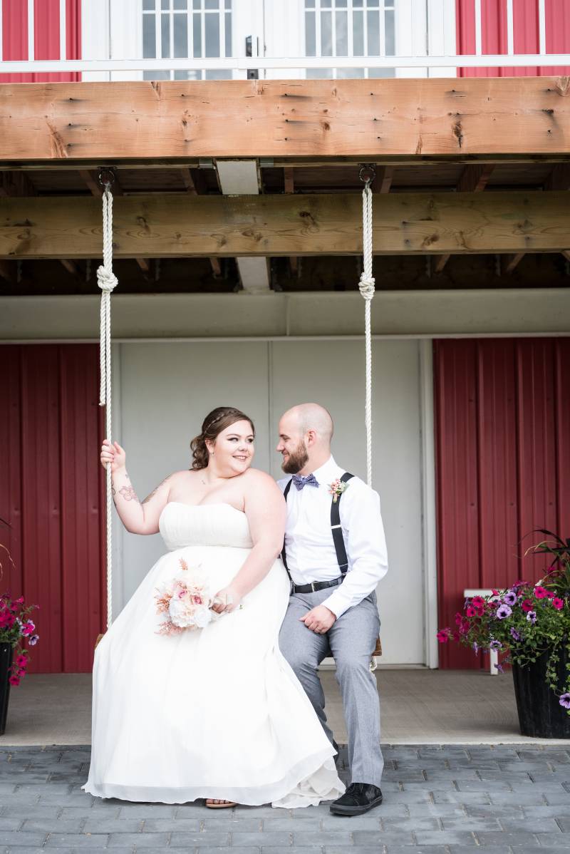 Bride and groom sit together on swing smiling under balcony 