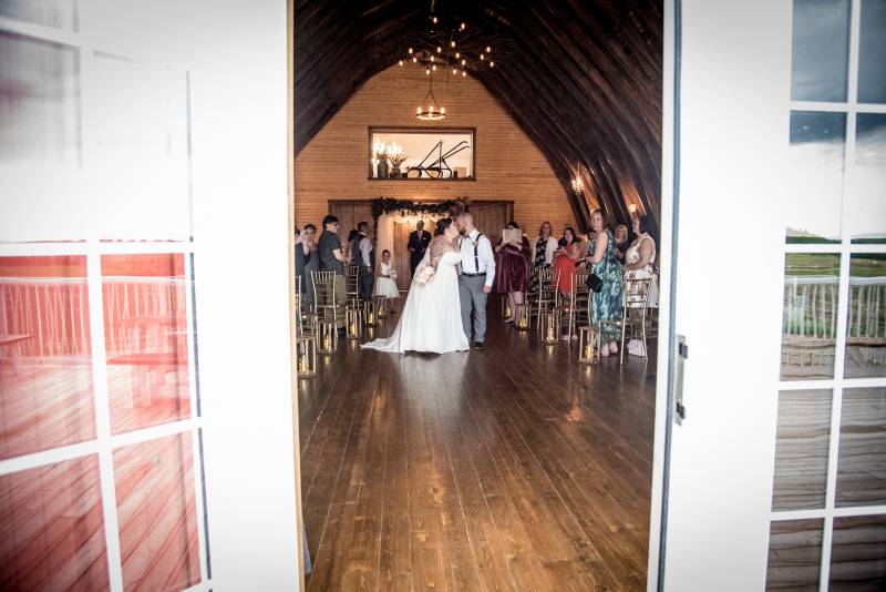 Bride and groom kiss in middle of aisle while guests watch 