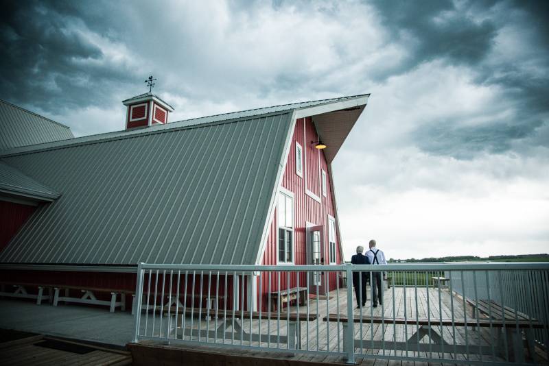 Couple walking on deck outside of red barn with white roof 