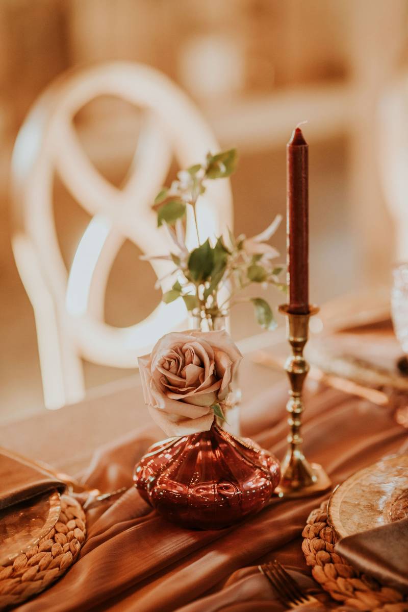 Blush rose in pink gold vase on blush table runner beside candlestick 