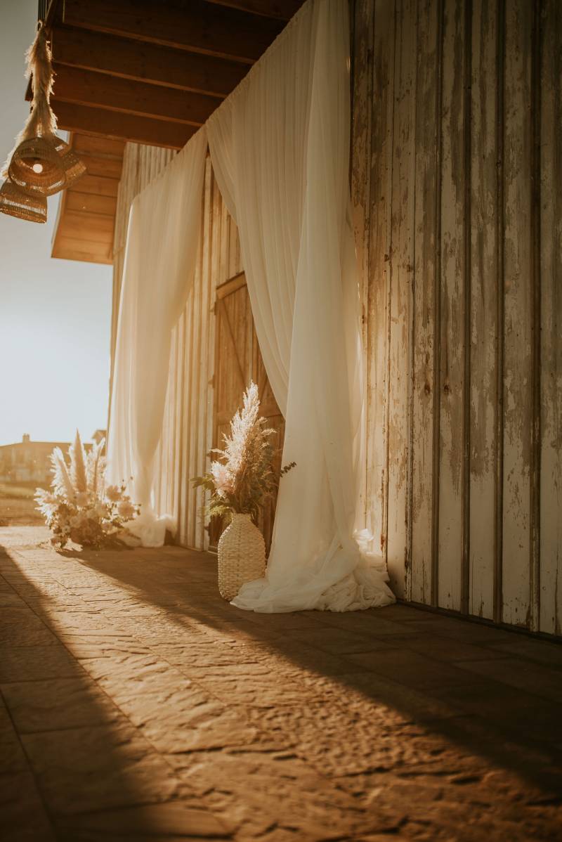 Old wooden barn with white curtains opened over doorway at sunset 