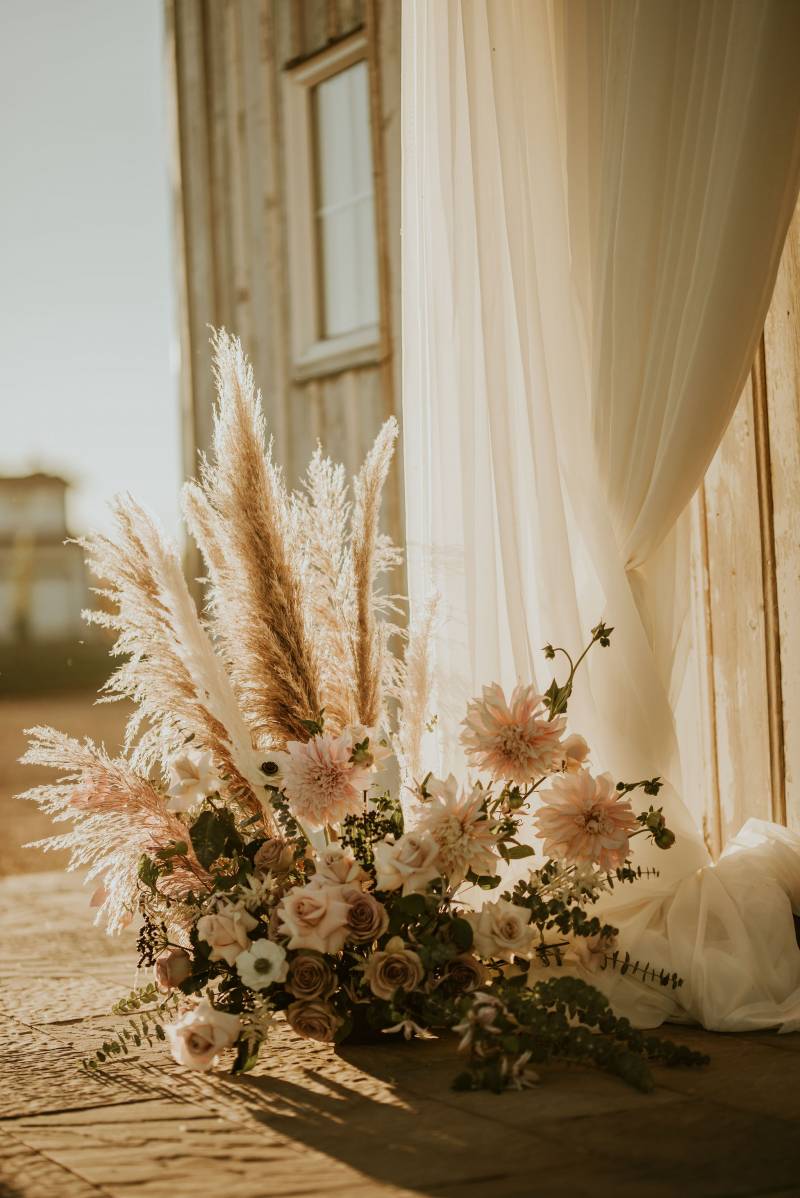 Pampas grass and white and blush flower arrangement beside white draping fabric 