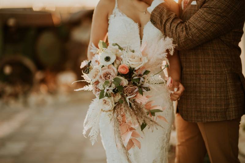 Bride in white lace dress holding blush and white bouquet beside groom 