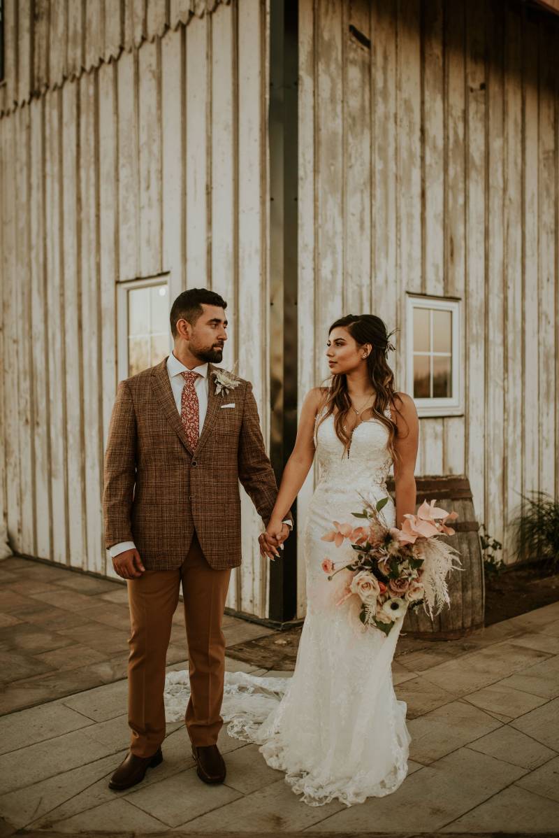 Bride and groom stoic faces holding hands at corner of barn 