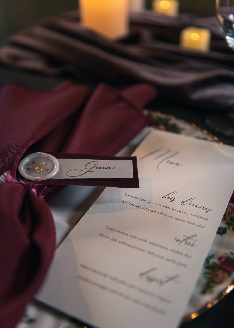 Wedding reception menu beside burgundy napkin labelled groom