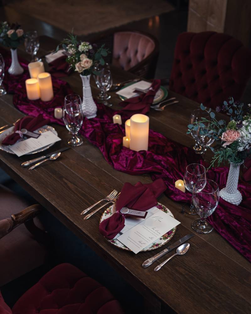 Large brown table with burgundy table runner and candles with white vase floral centerpiece 