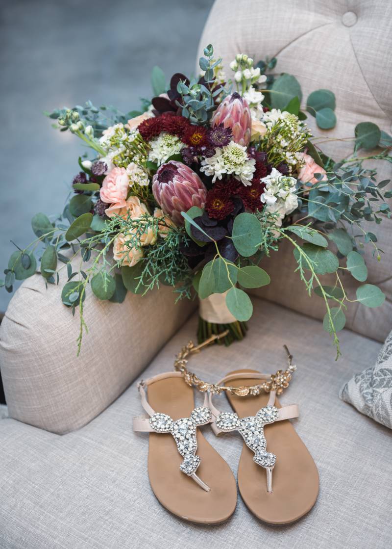 Burgundy and pink bouquet behind gold flower crown and brown strapped sandals 