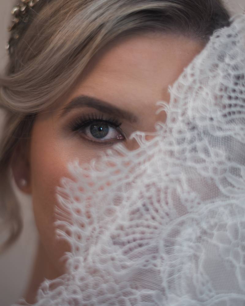 Bride peers from behind white lace dress 