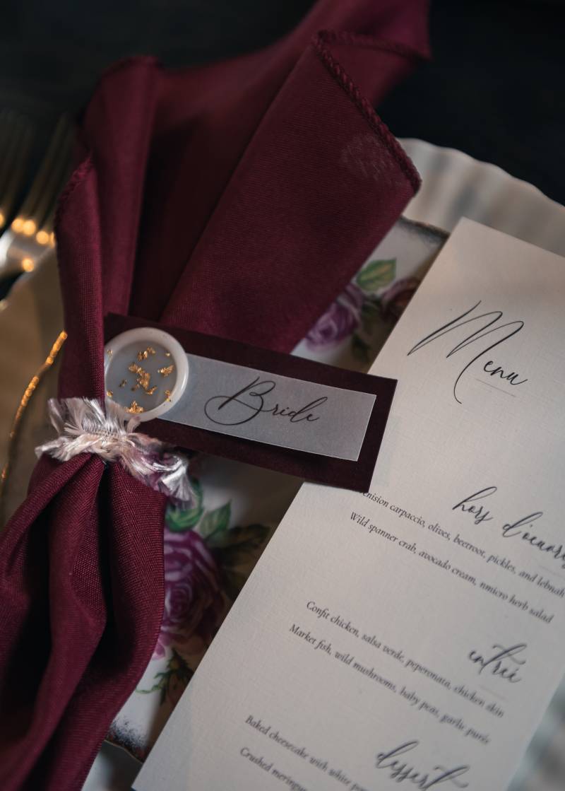 Wedding reception menu beside burgundy napkin labelled bride 