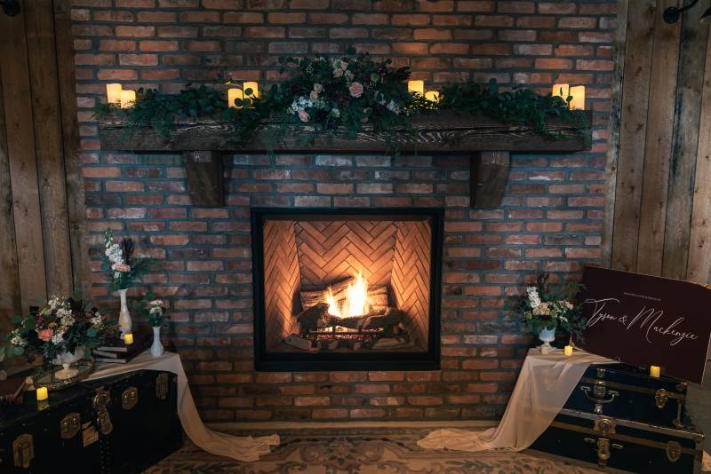 Brick fireplace with floral decorated mantle and suitcases with fabric and signs beside 