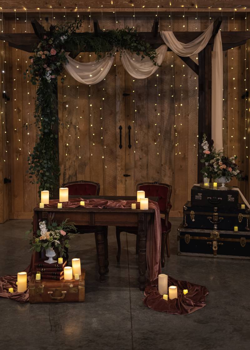 Table with long pink table runner and candles in front of dark wood wedding arch and fairy lights wall