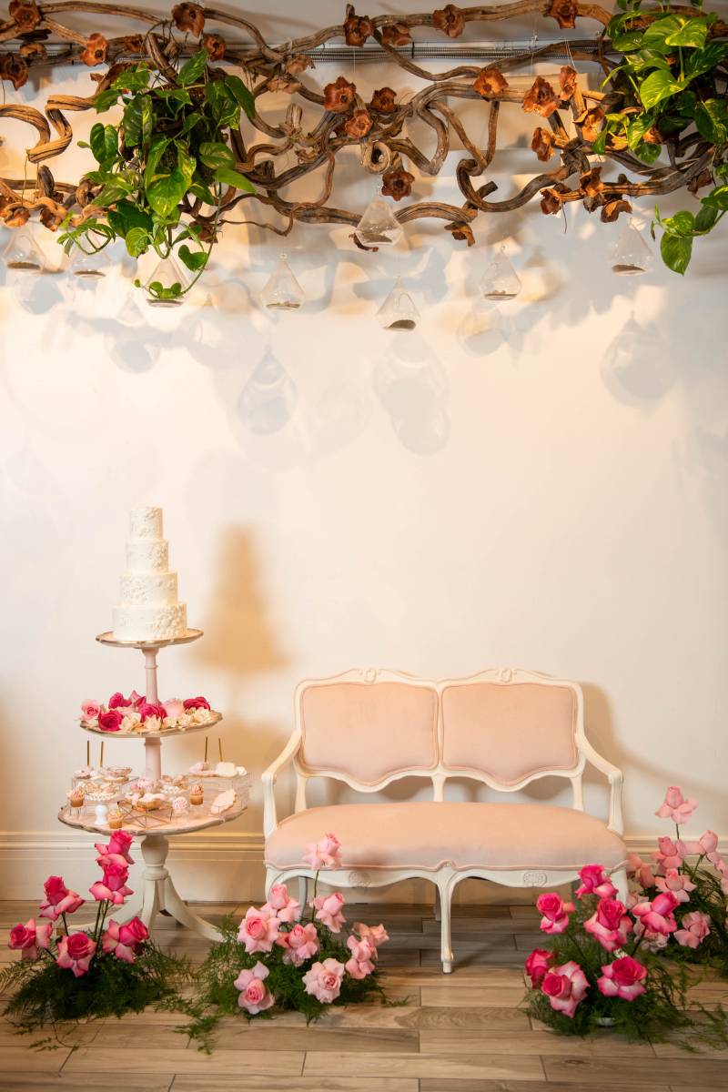 Blush pink sofa beside white wedding cake arrangement under wooden vines 