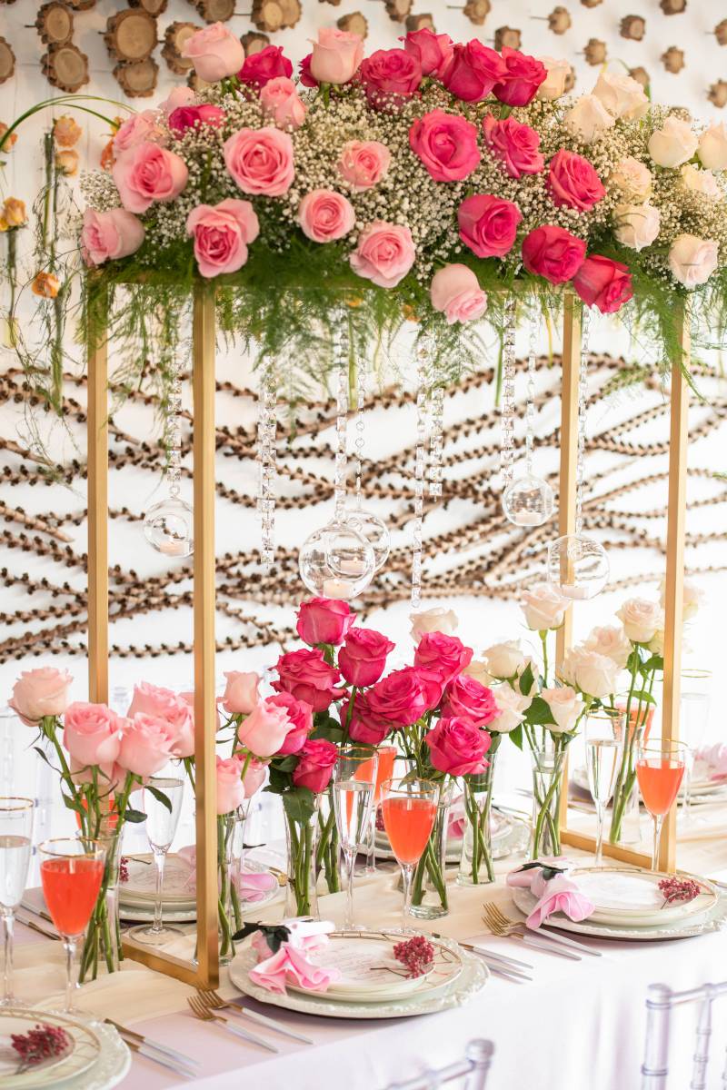 Table with pink and white table setting under gold arch with pink and white flowers above 