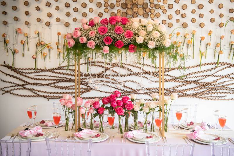 Table with pink and white table setting under gold arch with pink and white flowers above 
