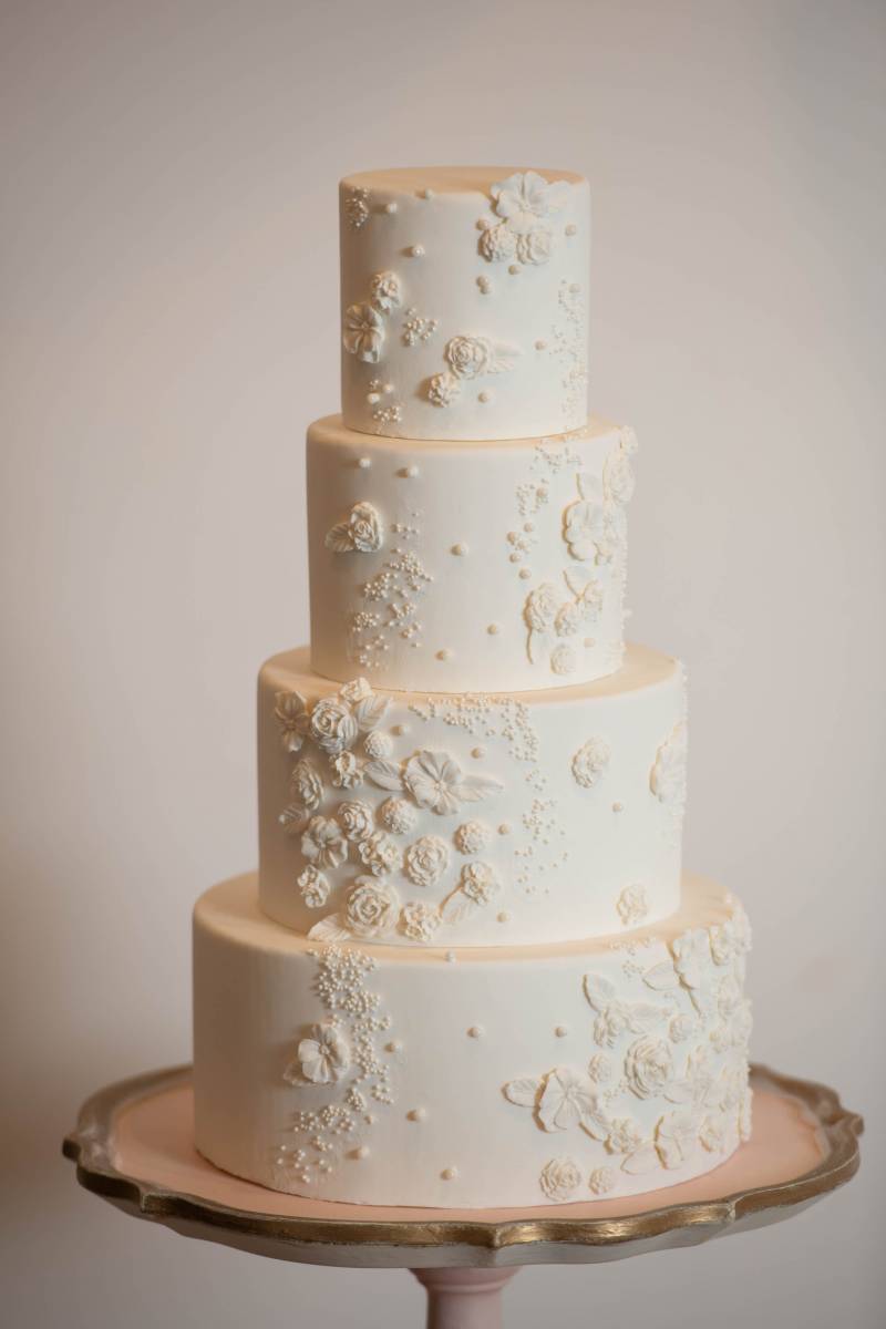 Four tiered white wedding cake with white floral accents 