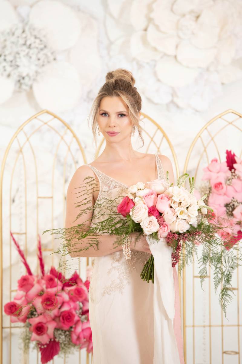 Bride standing in beige dress holding white and pink bouquet 